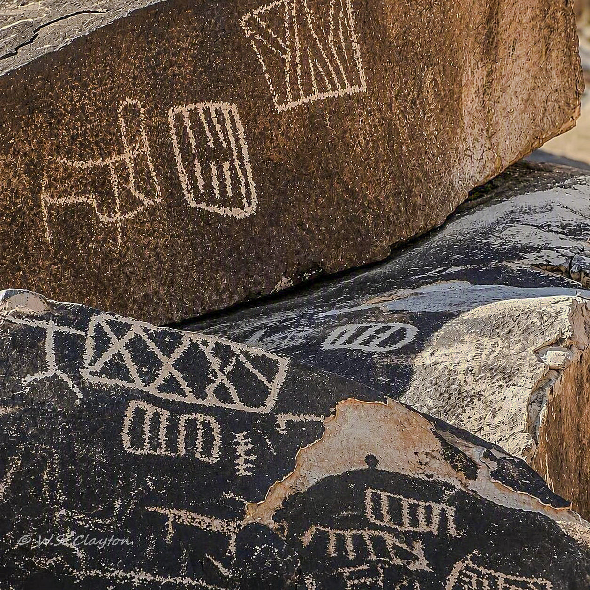 Close-up of engraved rock faces with pale geometric and figurative petroglyph-like markings on brown and black stone.